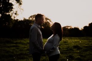 dark image of a couple standing and looking at one another with the sun setting behind them on a farm in Shropshire