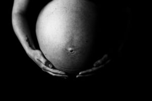 moody black and white photo of a pregnant belly with an arm wrapped around
