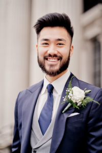 Groom portrait. Groom wears blue suit with large white flower button hole
