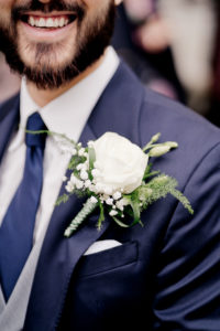 Large white flower button hole on groom's blue suit jacket