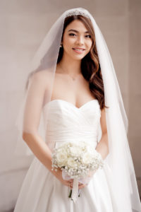 Bridal portrait of a bride dressed in a white dress, with white veil and tiara and holding a white floral wedding bouquet