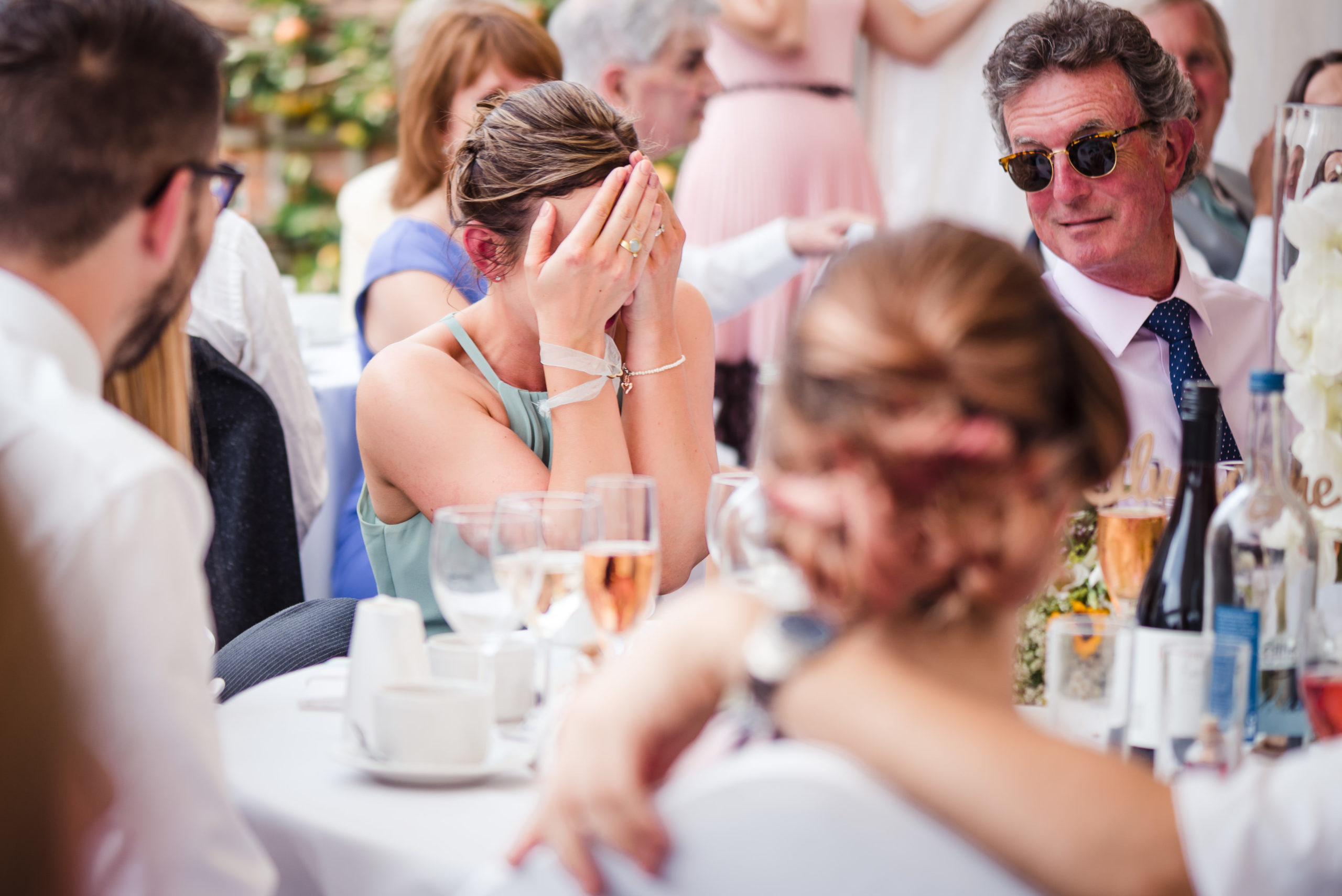 a bridesmaid holds her face in her hands as she is embarrassed about something someone said in a speech at a wedding