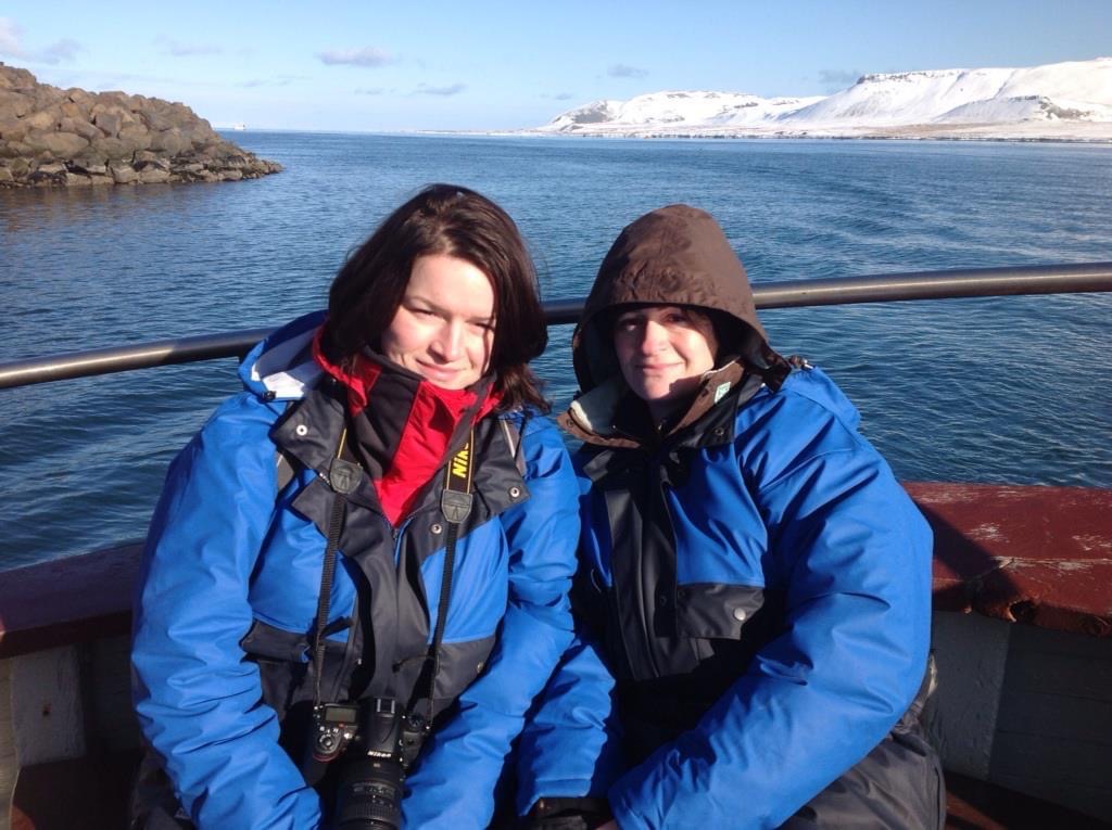 two women sitting on a boat in Iceland nicely wrapped up warm with the sea behind them