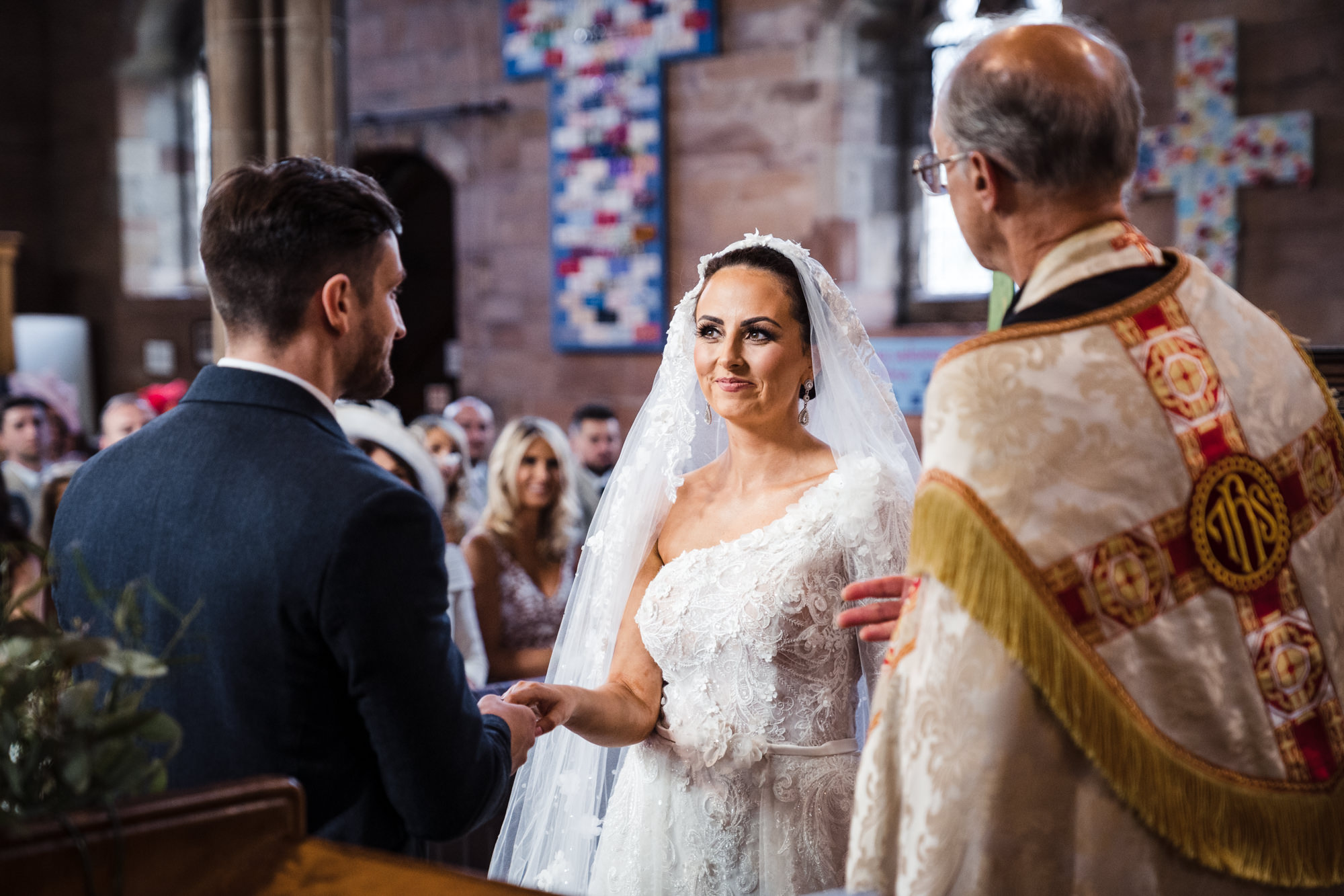 bride dressed in white looking at groom in church as they exchange vows