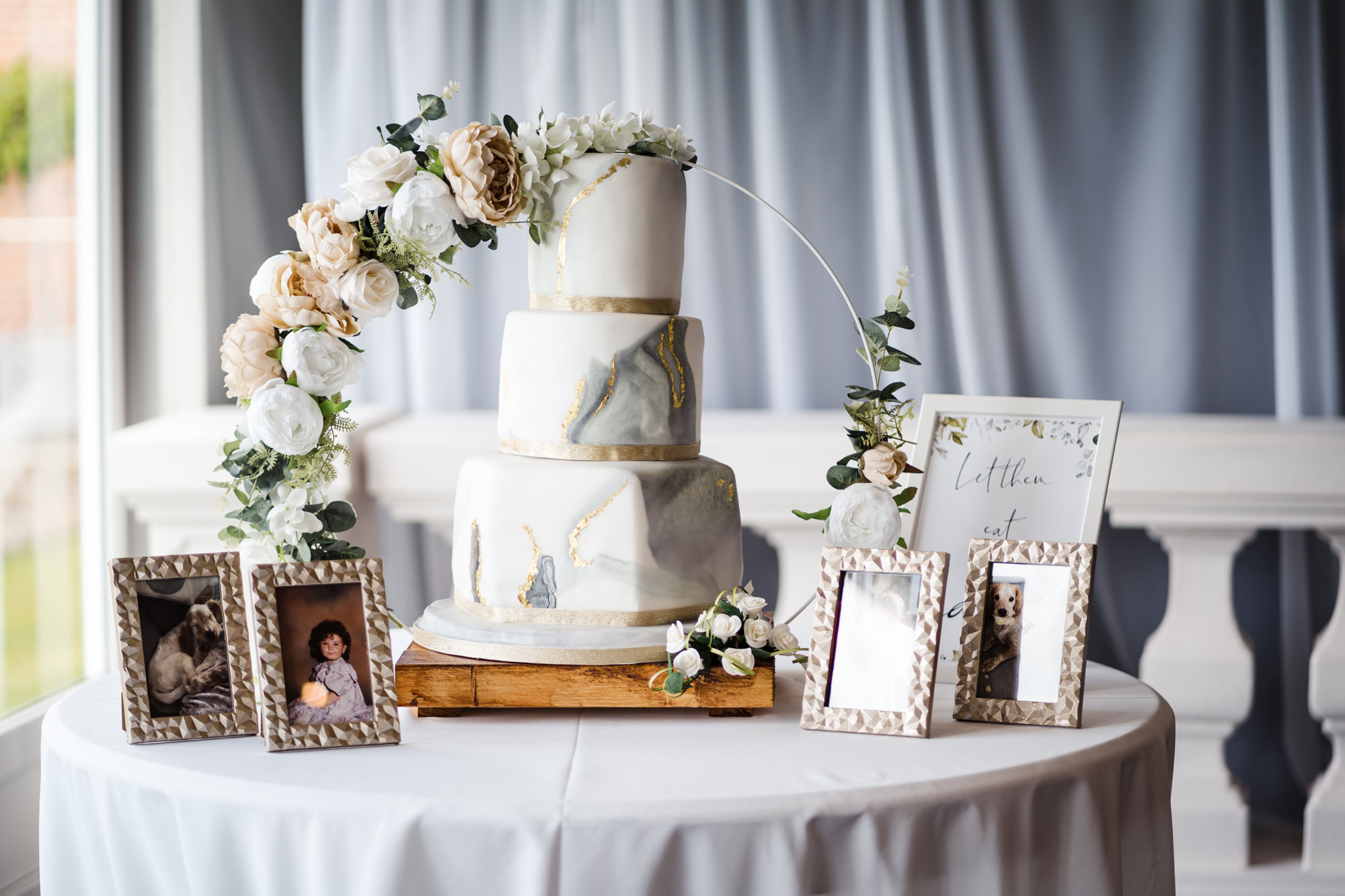 wedding cake with gold and grey details surround by a flower arch