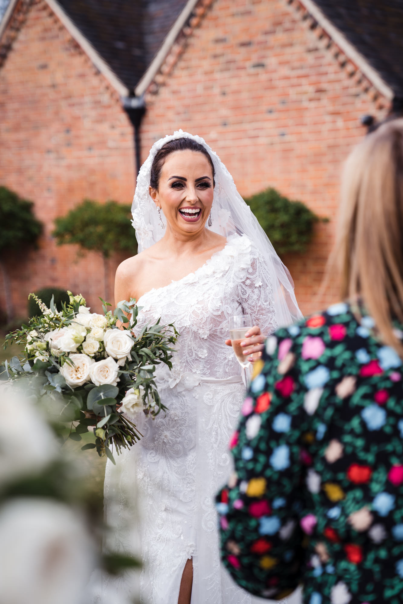 bride laughing at her wedding reception with guests holding her floral bouquet and a glass of champagne