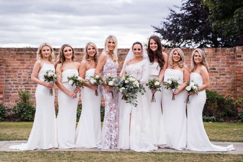bride in white dress with seven bridesmaids all wearing floor length white dress and green and white flower bouquets