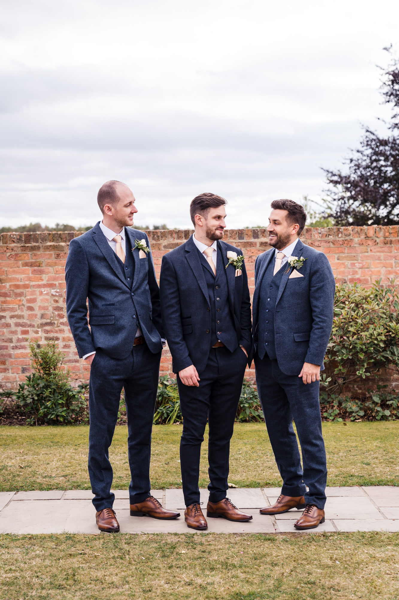 groom in a blue suit stood smiling with tow best men and flower button hole detail