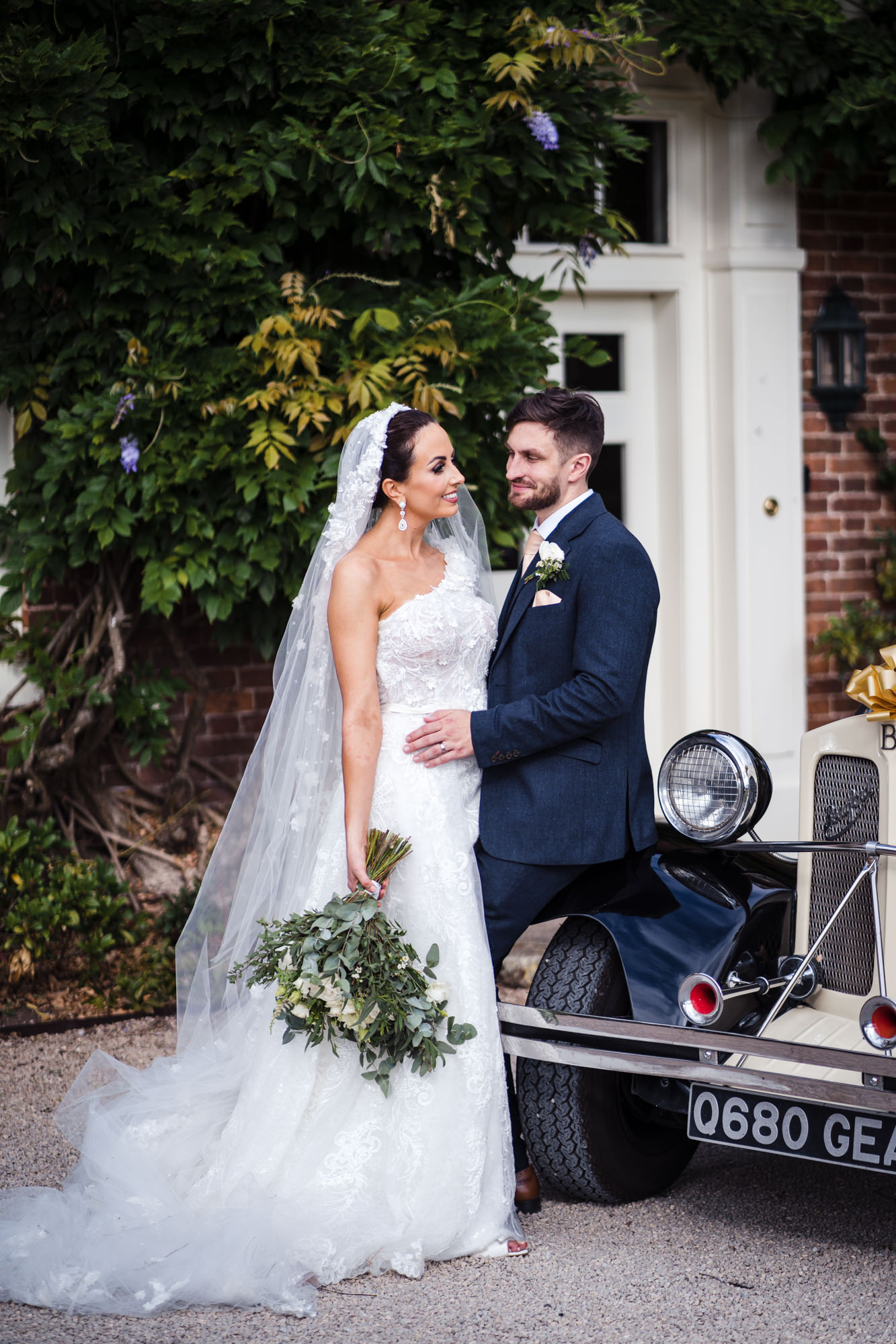 bride and groom embrace leaning against classic wedding car at wedding venue