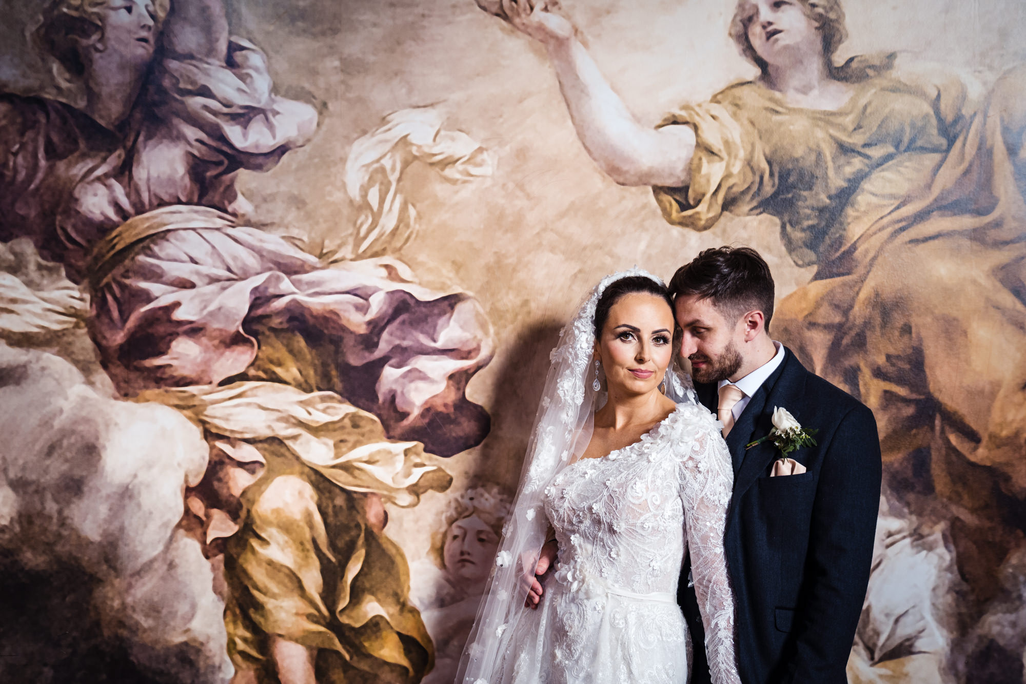 bride and groom pose in front of large renaissance wall mural