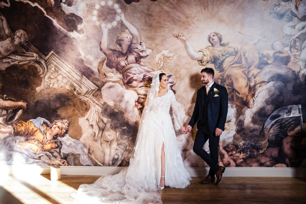 full length photo of bride and groom in front of renaissance wall mural at alrewas hayes wedding venue