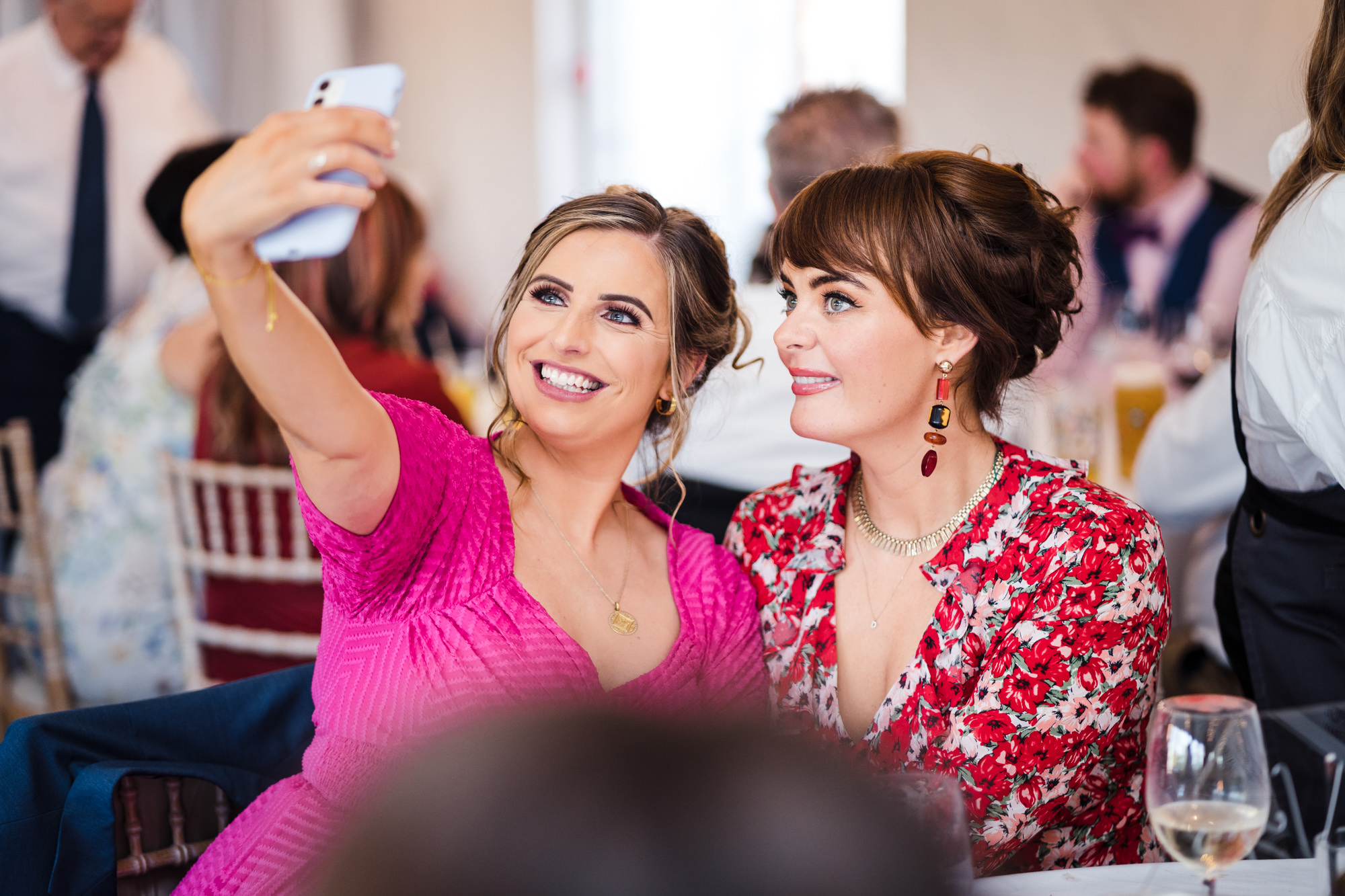 two female guests at wedding pose and smile for a selfie