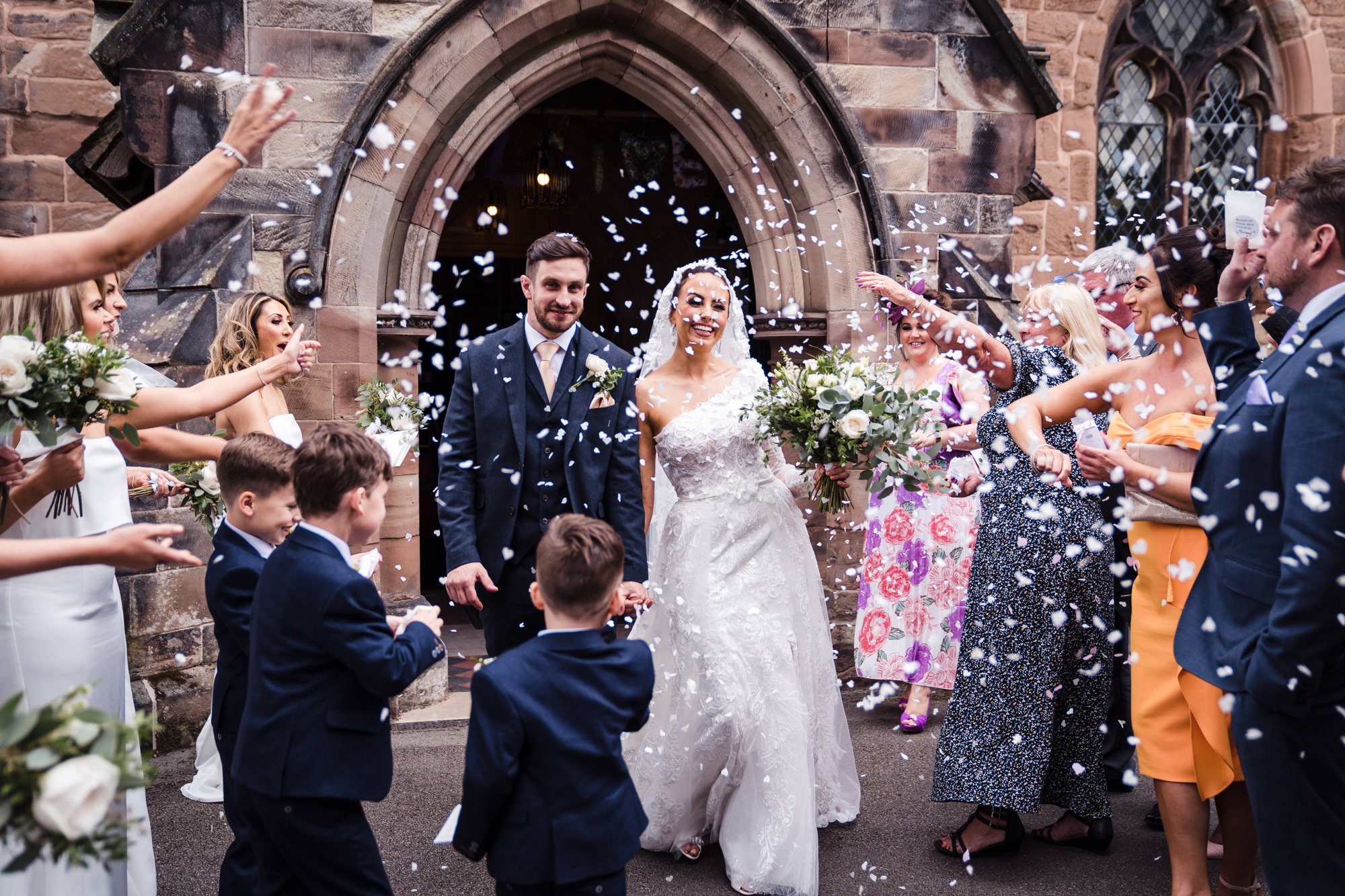 bride and groom looking happy as they walk through confetti outside a church