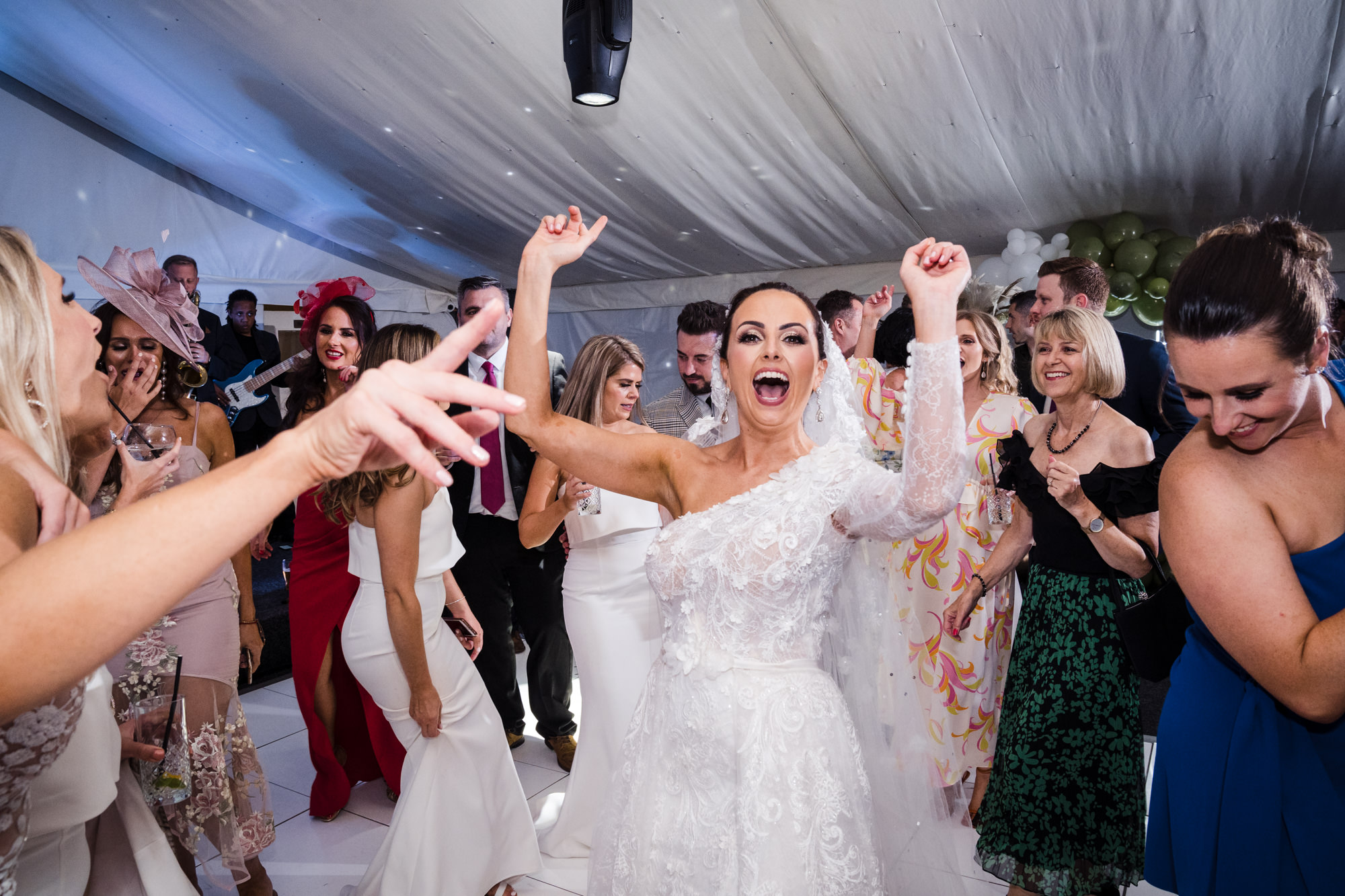 bride with arms in the air and cheering as she dances with wedding guests
