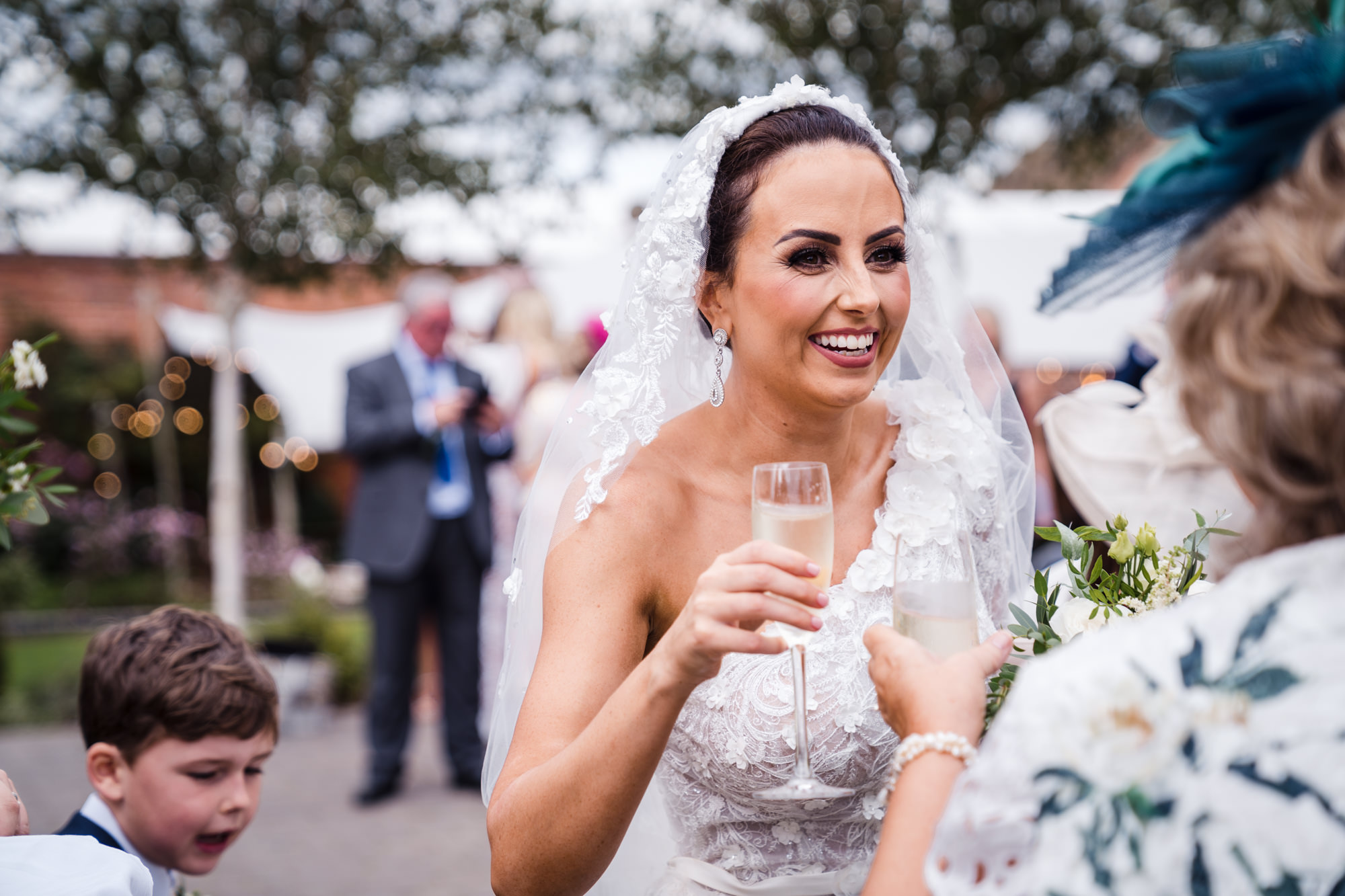 bride dressed in white holding a glass of champagne and smiling with a wedding guest