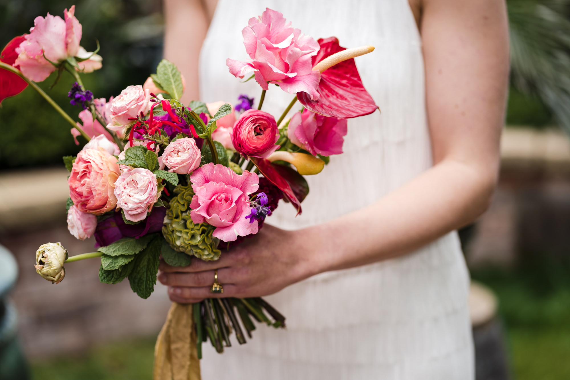 bride wears short white wedding dress and holds a pink and red bold colourful wedding bouquet