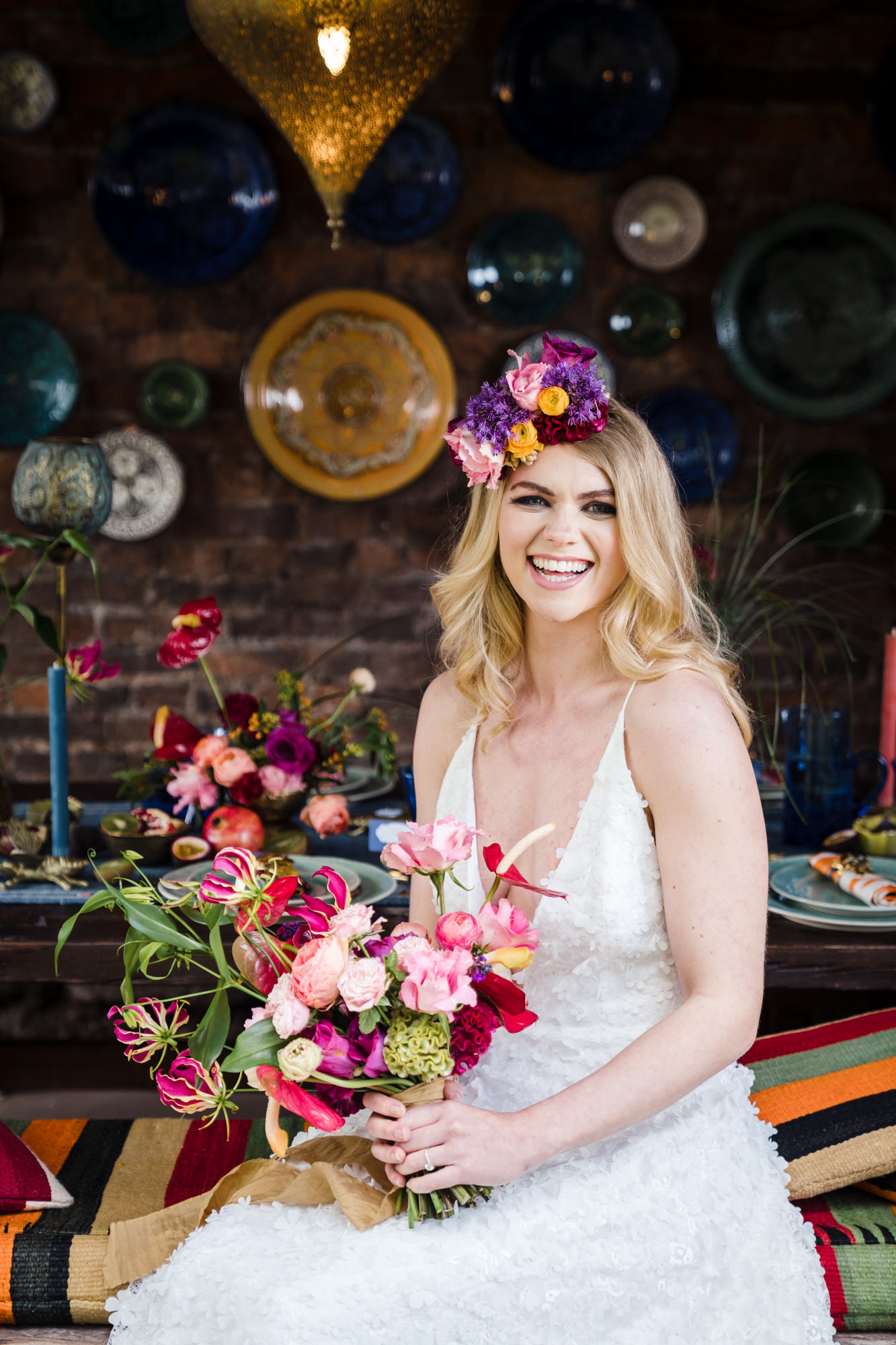 stunning bride smiles at the camera wearing a long white wedding dress from charlie brear holding a colourful bouquet and wearing a statement head crown
