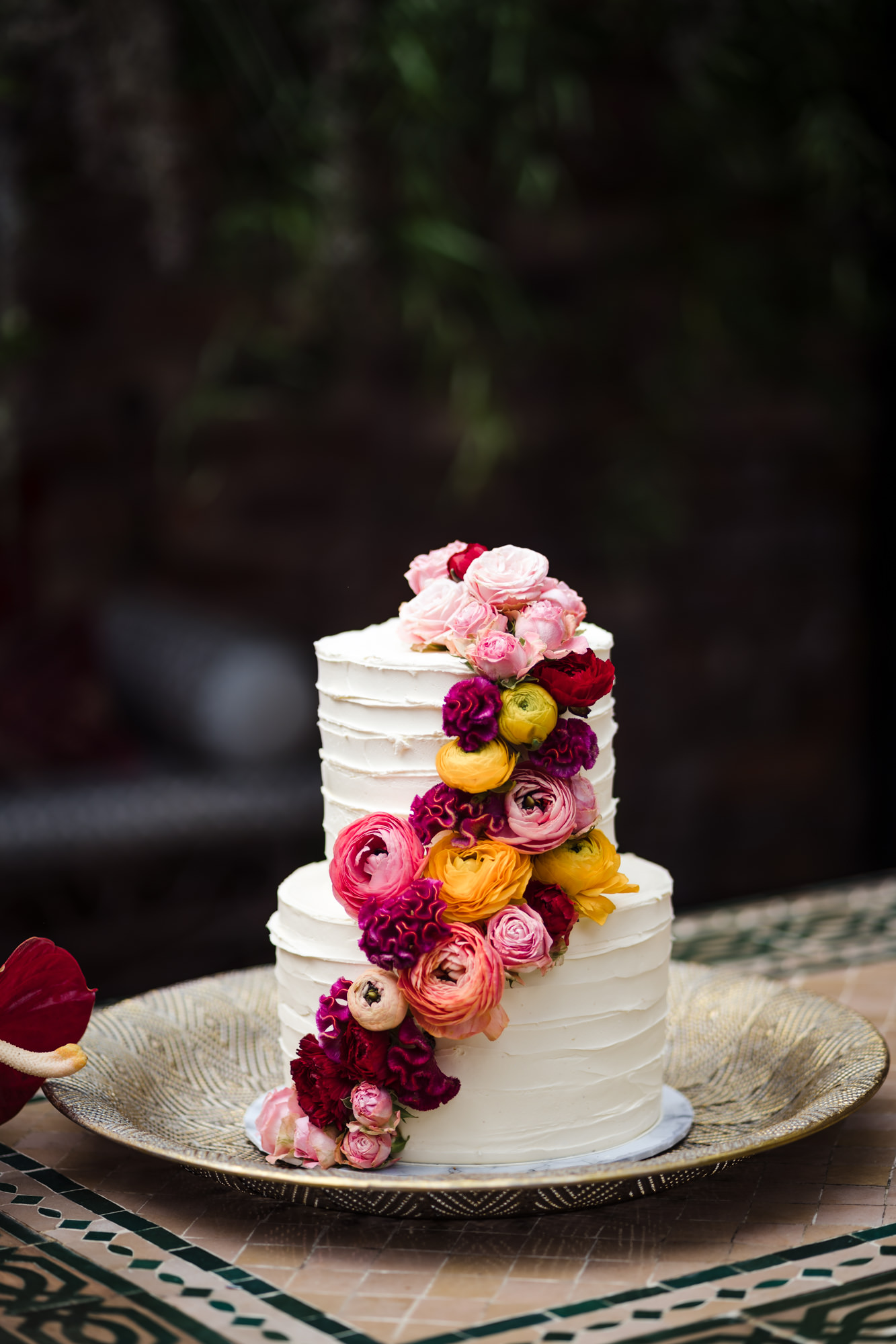 white two tiered wedding cake decorated with pink red yellow flowers