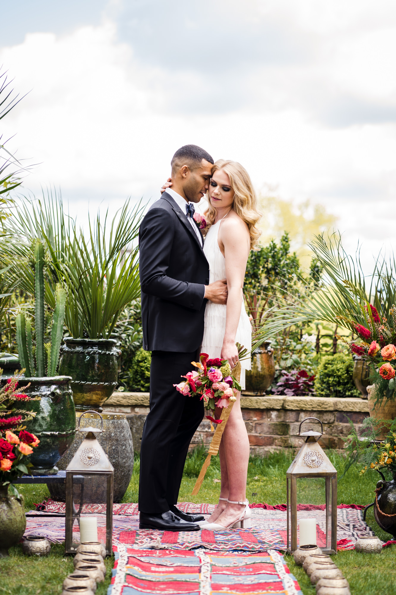 a bride dressed in a short white wedding dress from Charlie Brear hugs a groom wearing a black tie suit and bride holds a colourful bold flower bouquet