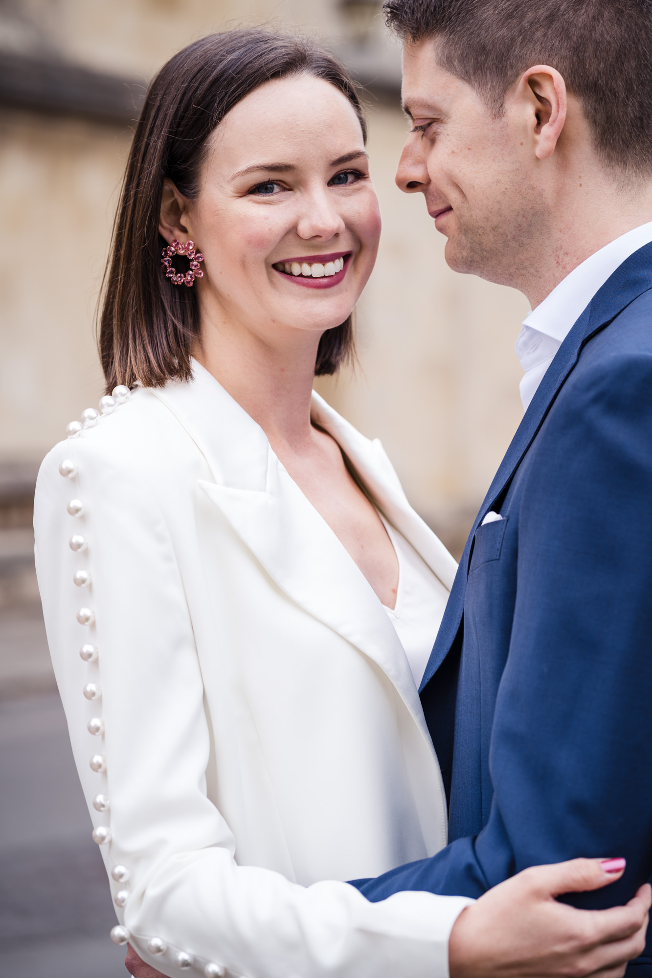 bride and groom portrait. bride smiles at the camera wearing a white Nadine Merabi Bridal Suit with pearl detail and pink earlings