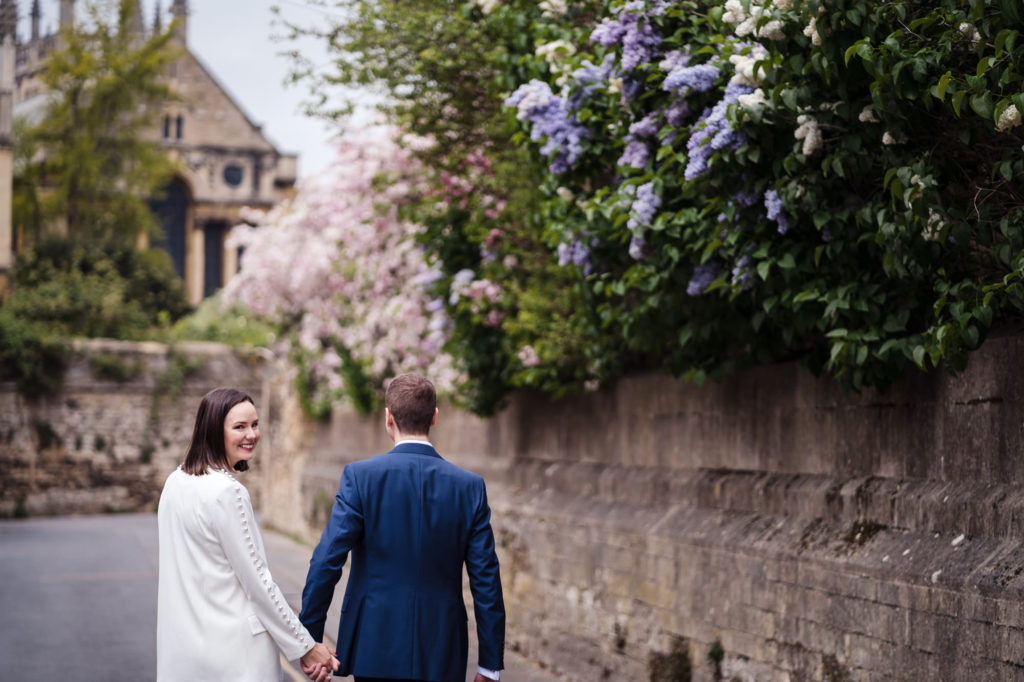 bride glances back over her shoulder as she walks with her husband through oxford after their registry office wedding