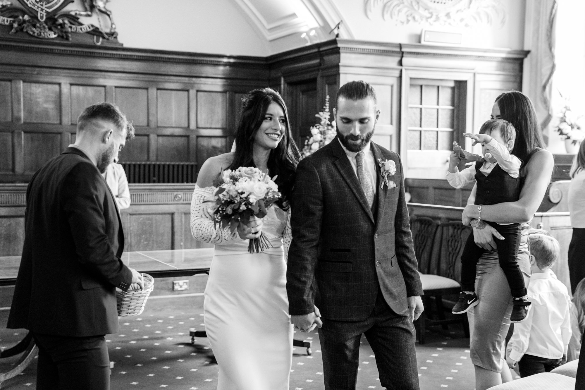 bride and groom leave the ceremony hand in hand and bride looks at groom in black and white image