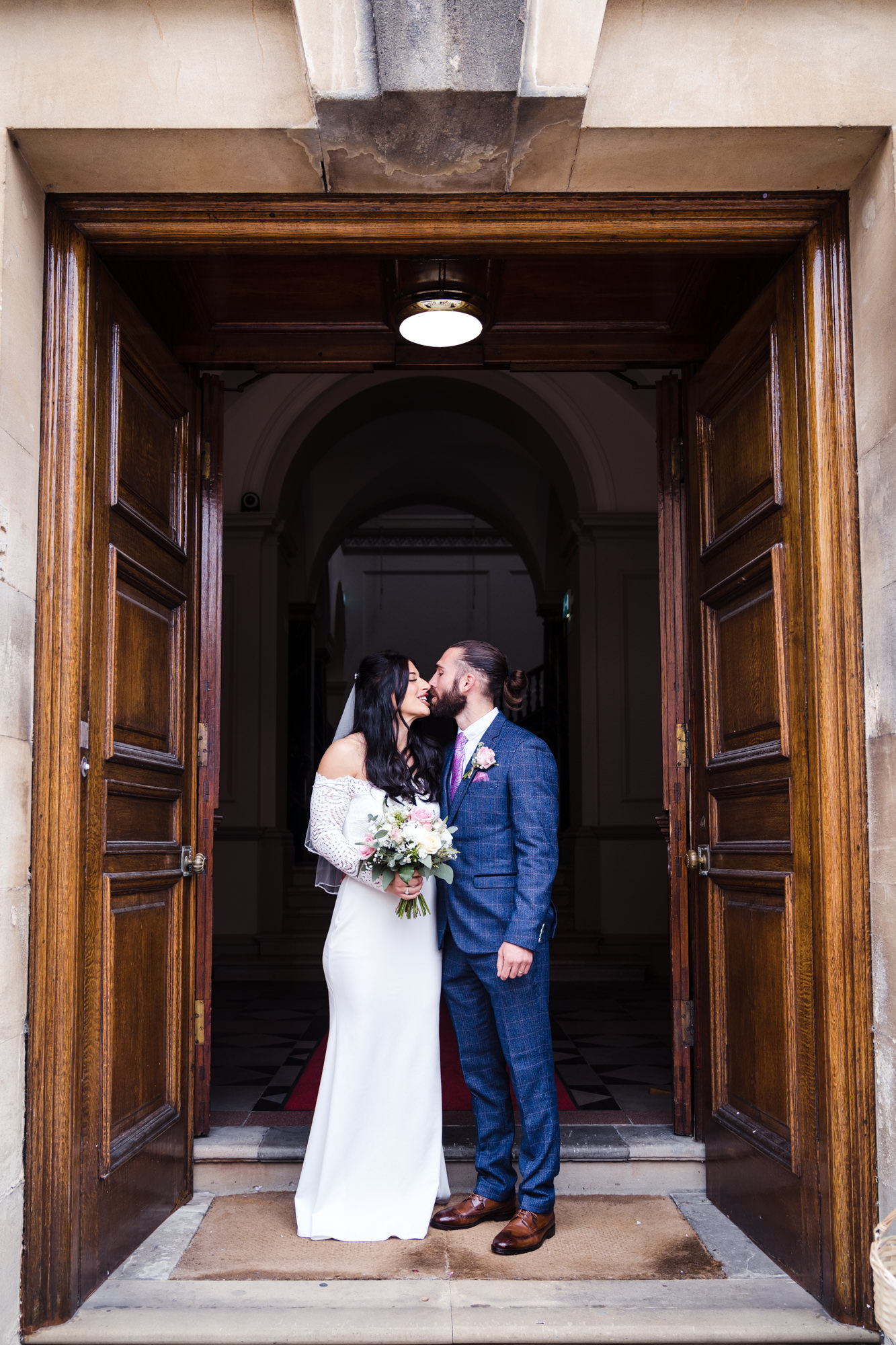 bride and groom pose for a picture as they exit the bath guildhall underneath a tall wooden door