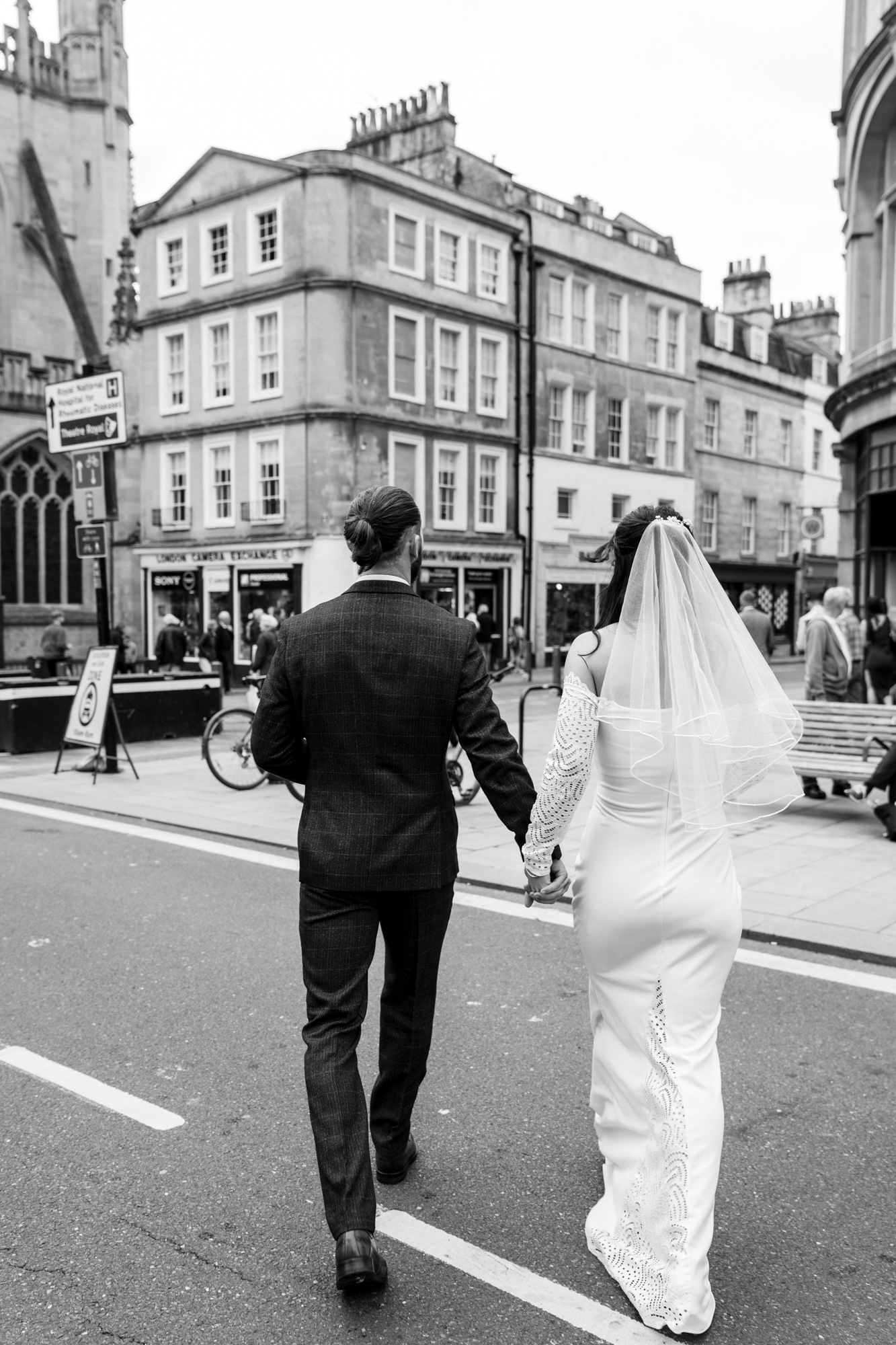 bride and groom hold hands and walk towards bath city centre in black and white photo