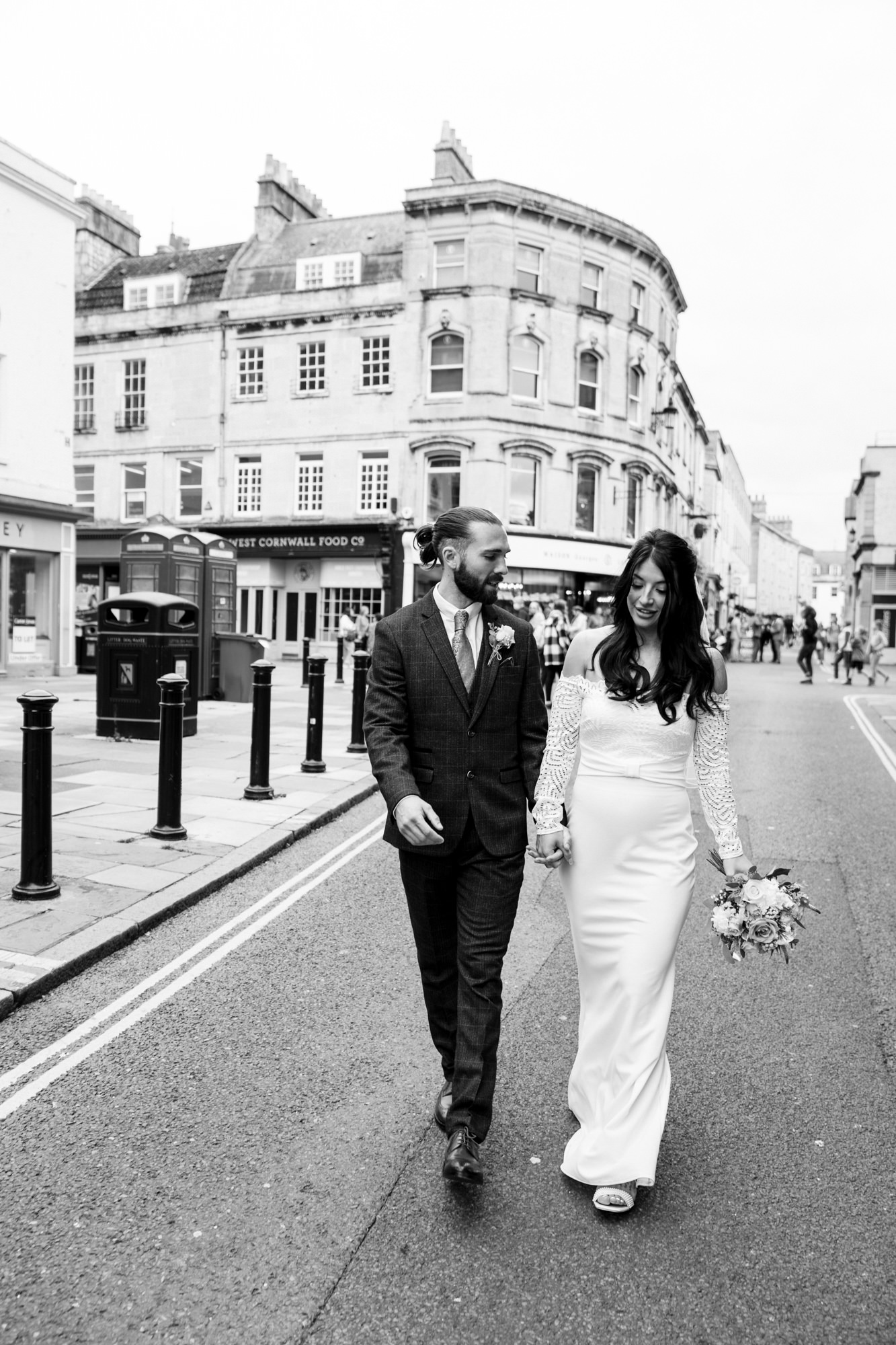 black and white image of bride and groom walking through the city centre of Bath as bride holds bouquet