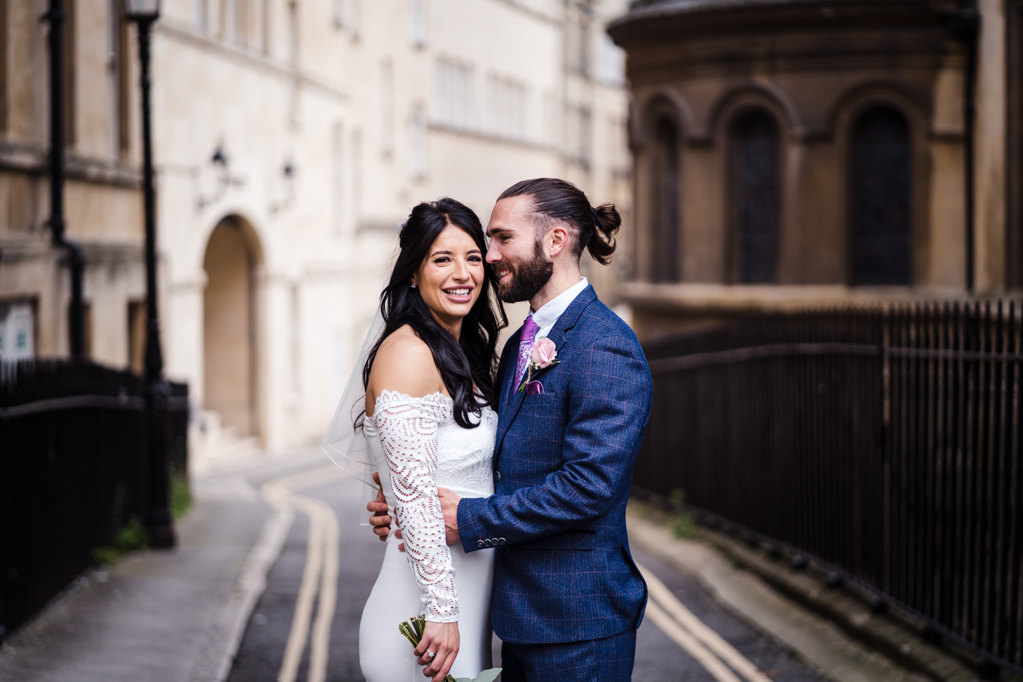 bride looks at the camera smiling as groom kisses cheek during couple photo shoot in bath
