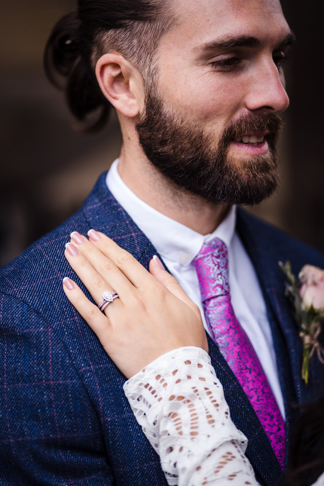 close up photo of brides hand resting on grooms shoulder showing off engagement and wedding ring