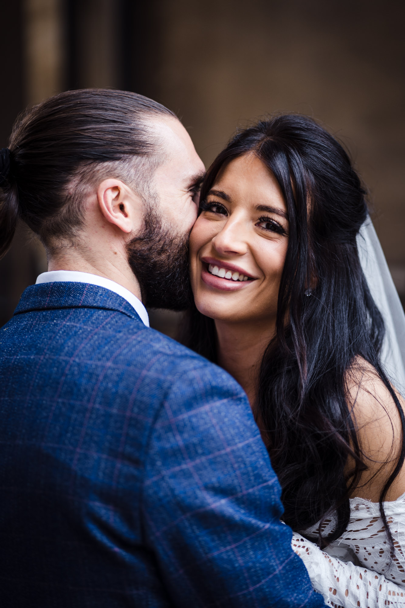beautiful bride smiles directly at the camera as groom whispers in her ear