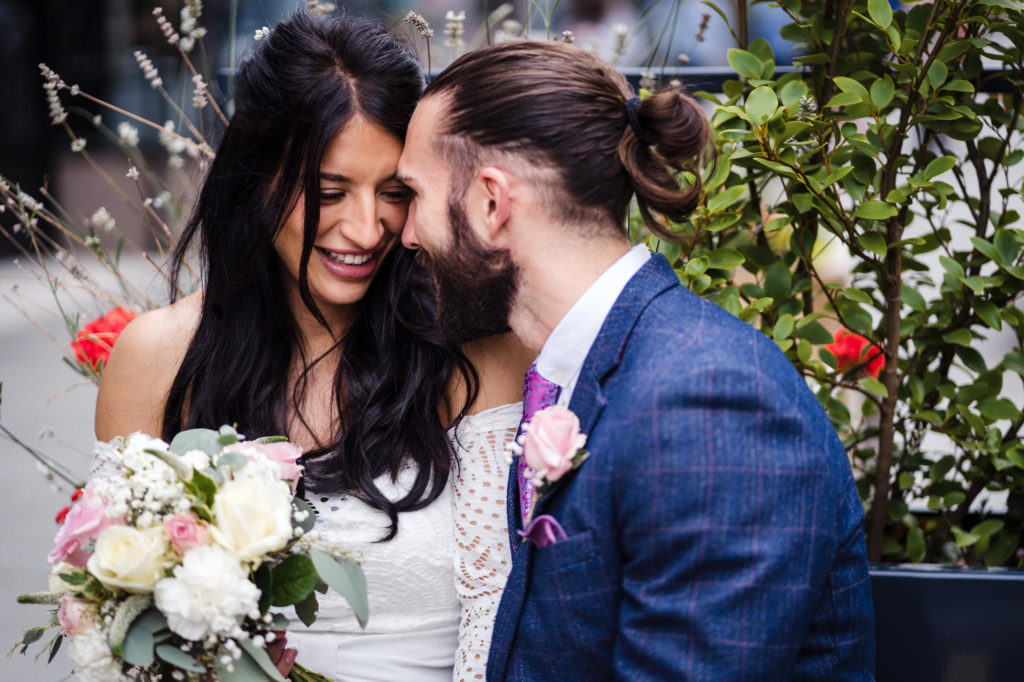 bride with long dark hair smiles as groom in blue suit kisses her
