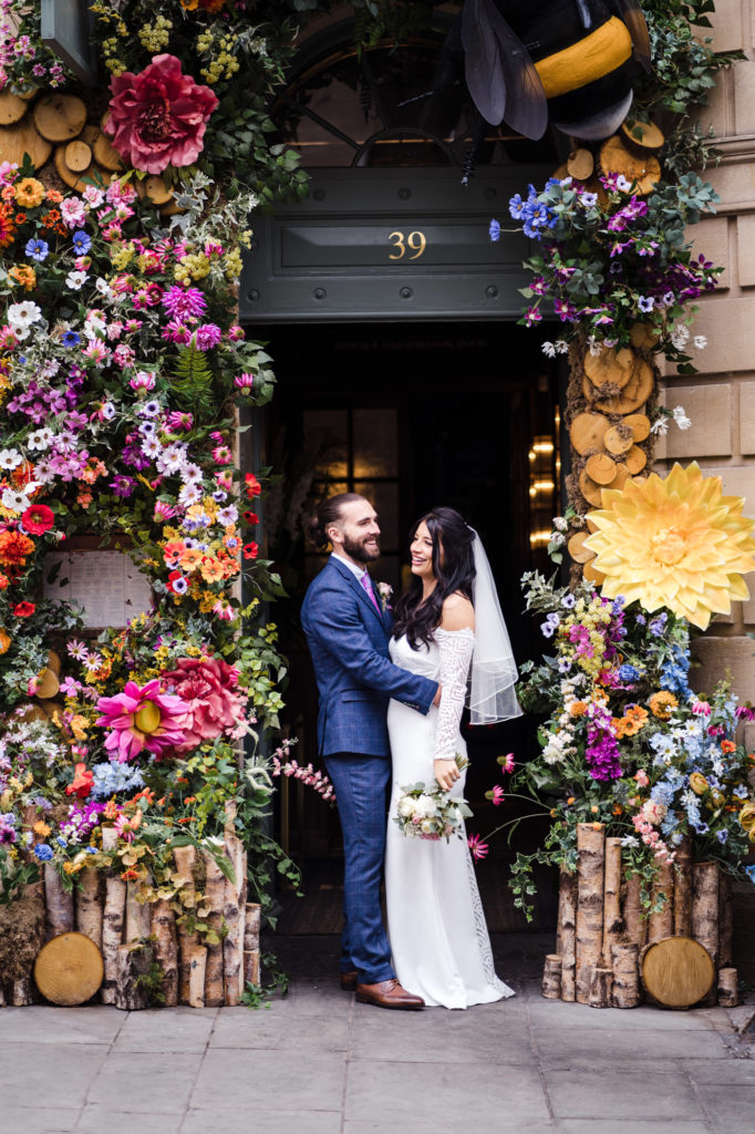 bride and groom pose for couple photo underneath colourful floral arch at the ivy restaurant bath