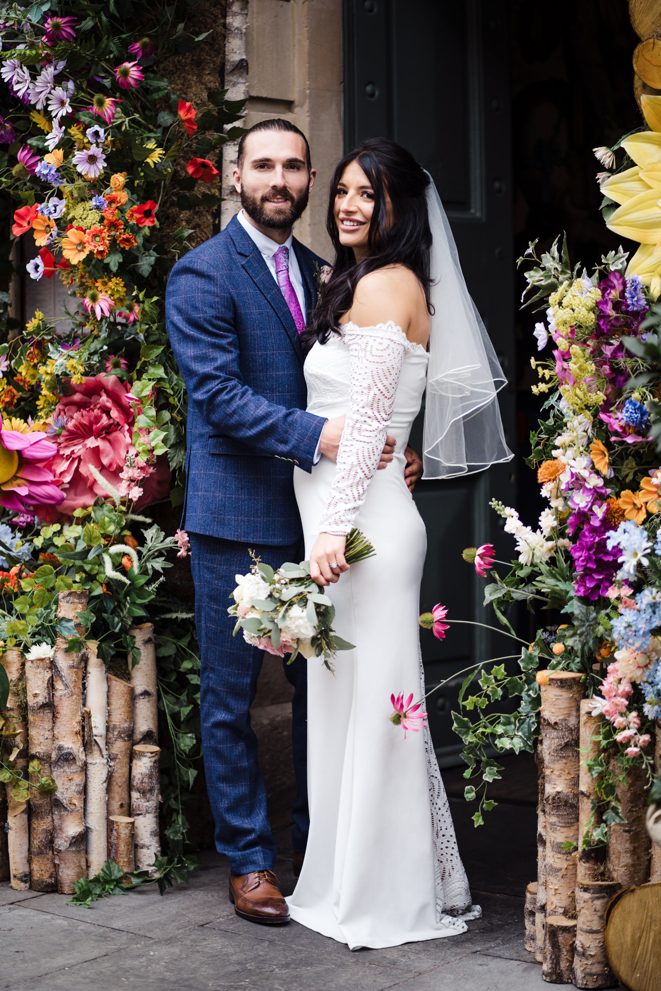 stunning bright bold flower arch with couple underneath posing for a couple photo