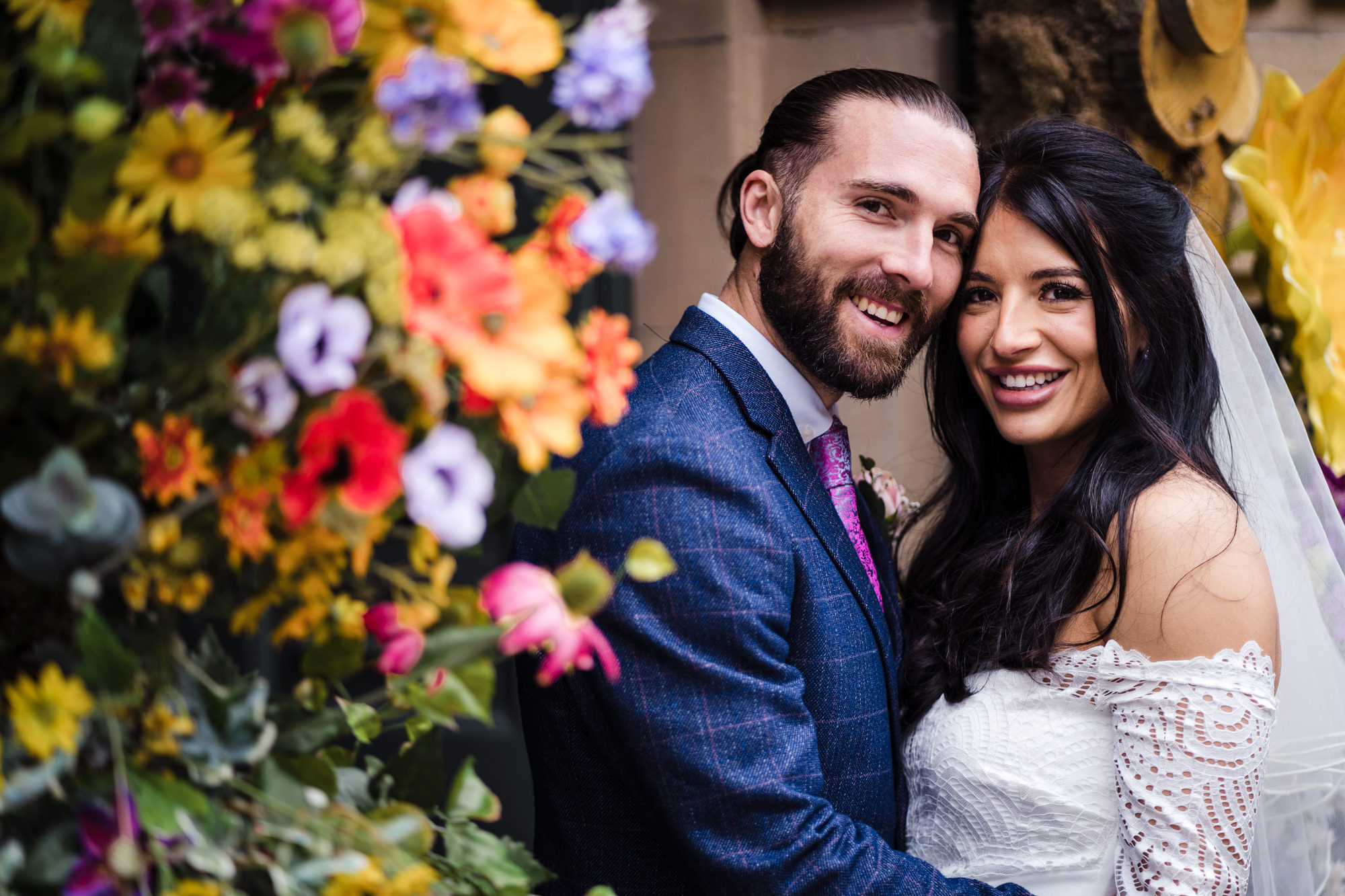 bride and groom smile at the camera for a photo with bright bold flowers at the ivy bath next to them