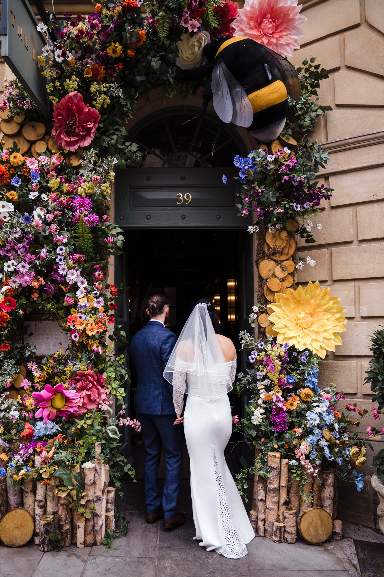 bride and groom walking into the ivy bath with big bold beautiful colour flower arch surrounding the door