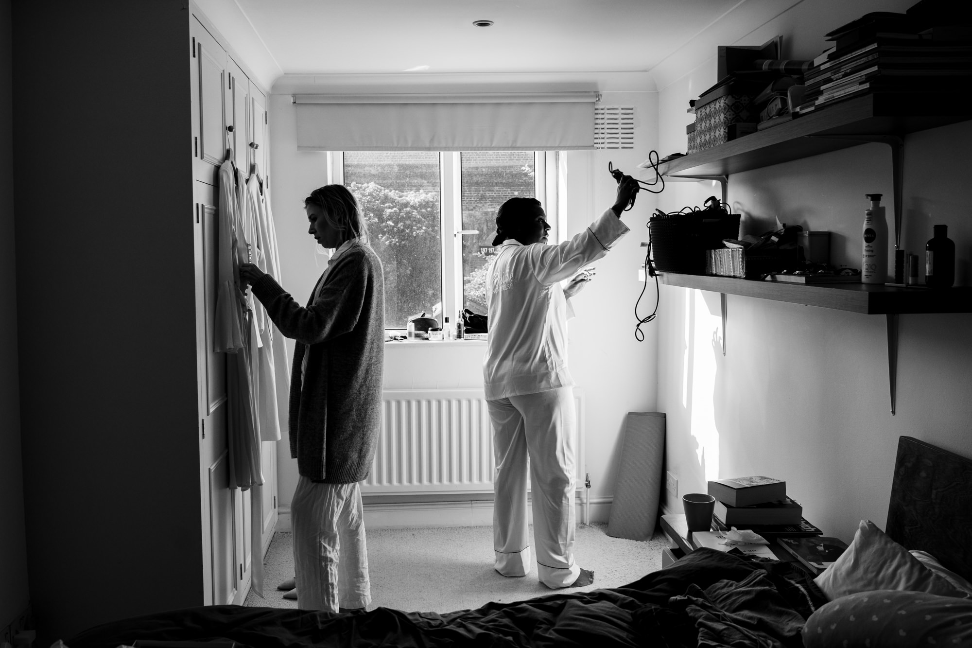 black and white photo of bride getting ready for her wedding as bridesmaid adjusts hanging dress on wardrobe
