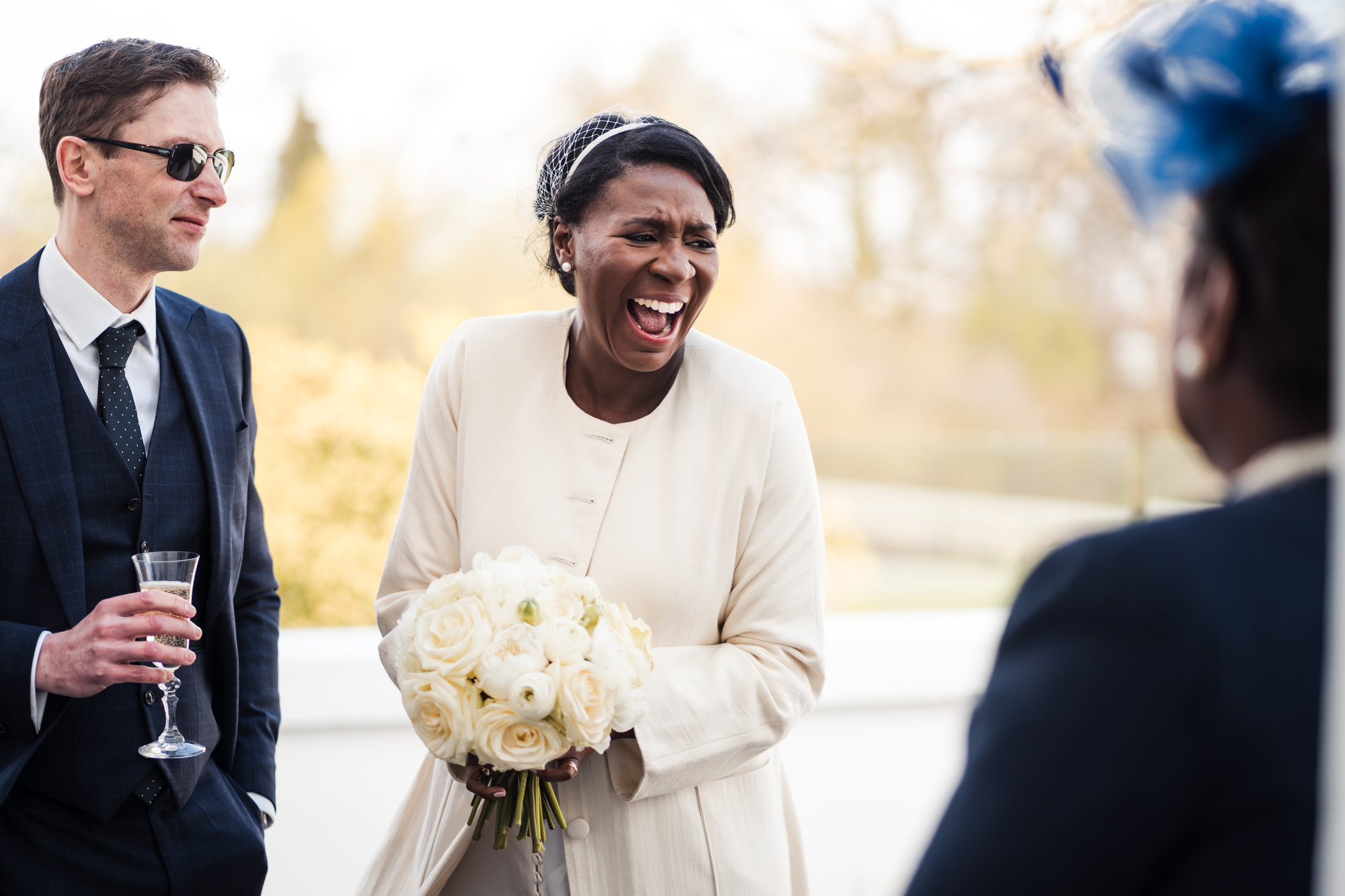 bride laughs at guests and groom looks admiringly at her holding a glass of champagne during the wedding ceremony