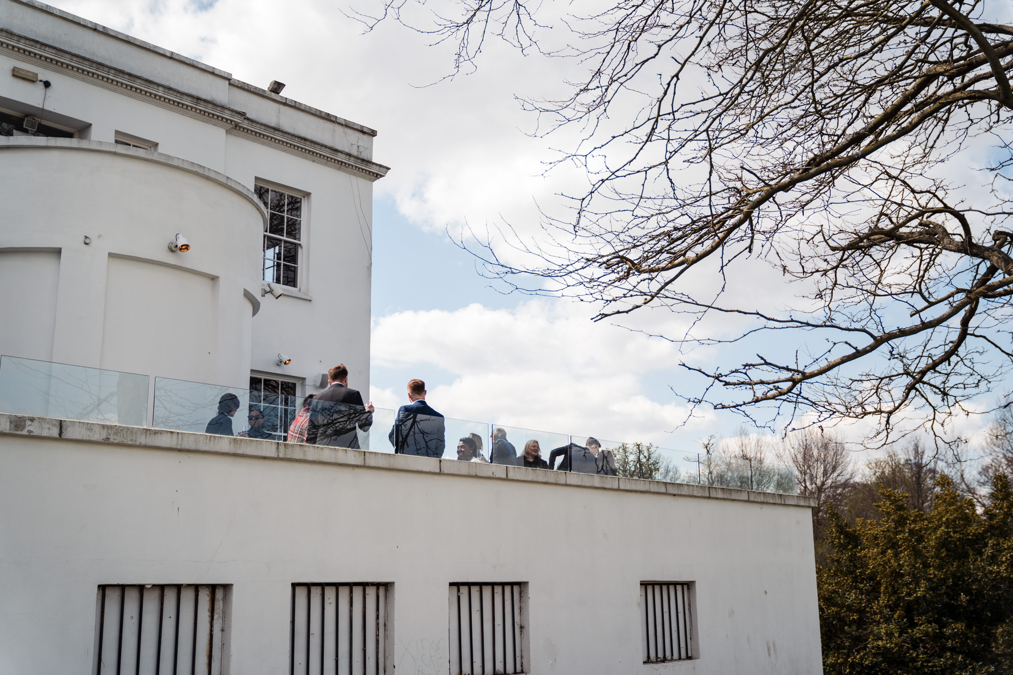 wide shot of guests enjoying a wedding drink reception on the balcony of belair house in south london