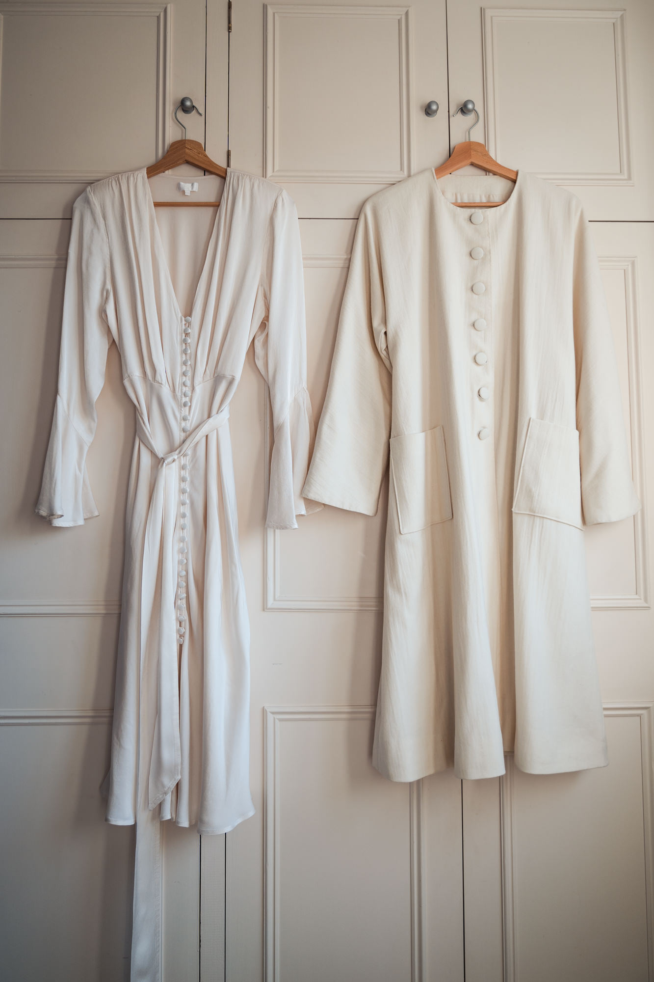 brides Ghost wedding dress hangs next to a cream bespoke jacket on a wardrobe