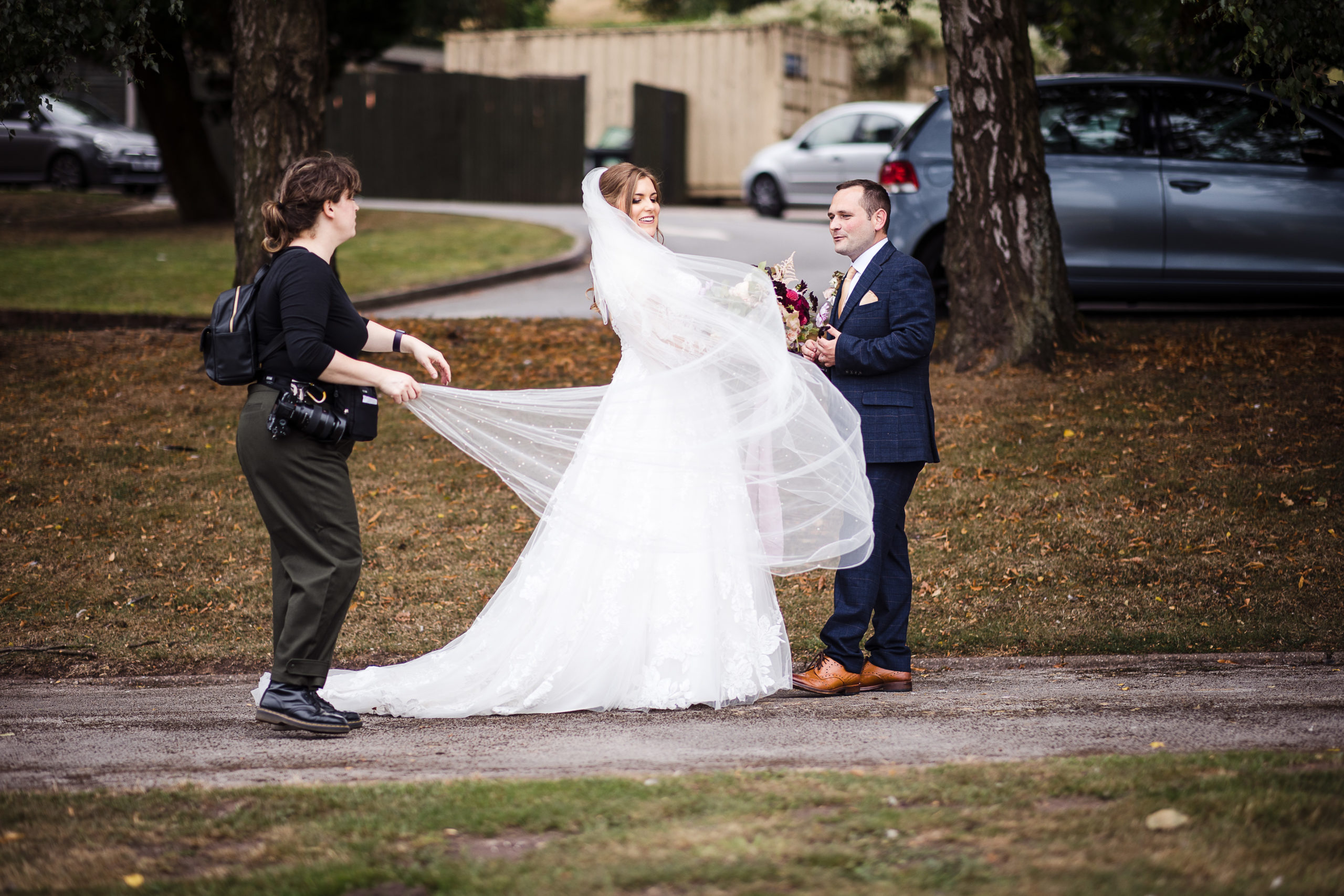 Laura May Photography adjusting a brides veil at a wedding before photographing her stood next to her husband
