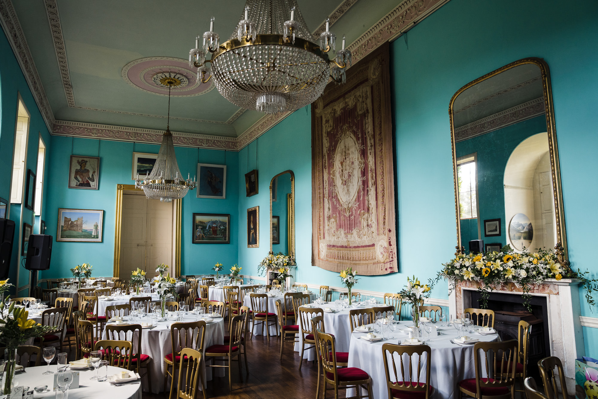 Walcot Hall teal blue dining room set for a wedding breakfast - round tables, floral centrepieces, chandeliers and tapestry