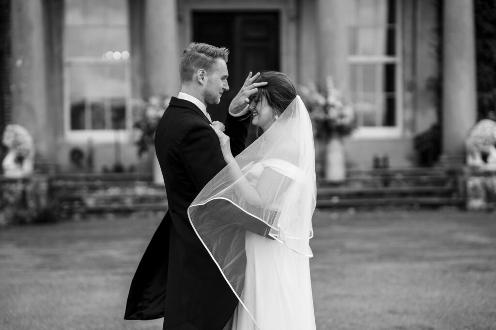 Classic black and white couple portrait, as groom brushes hair off brides face. Bride in off-shoulder Halfpenny London gown