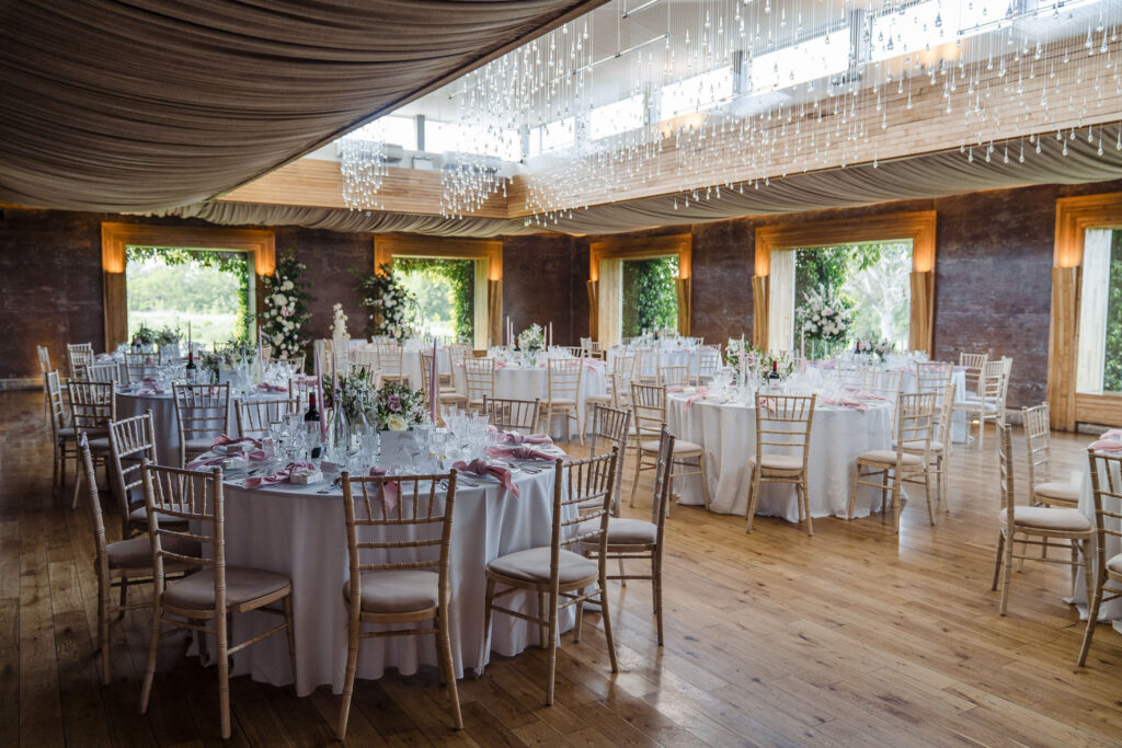 Elmore Court wedding reception room set for the wedding breakfast with round tables, floral centrepieces and draped ceiling lights.