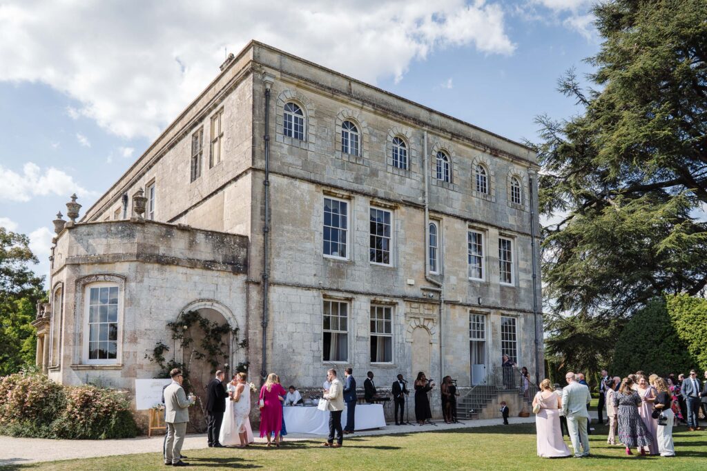 Elmore Court wedding venue exterior with guests mingling on the lawn during drinks reception.