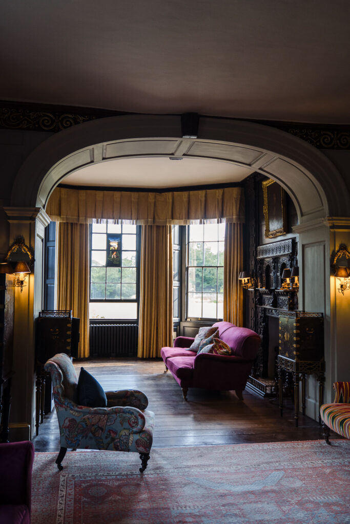 Moody lounge at Elmore Court with arched doorway, tall windows, velvet sofa and ornate fireplace
