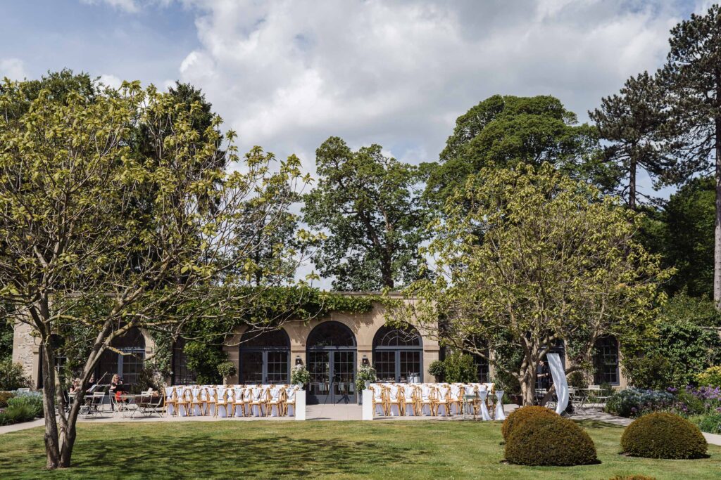 Outdoor wedding ceremony setup in the gardens at Middleton Lodge, with rows of wooden chairs in front of the arched orangery.