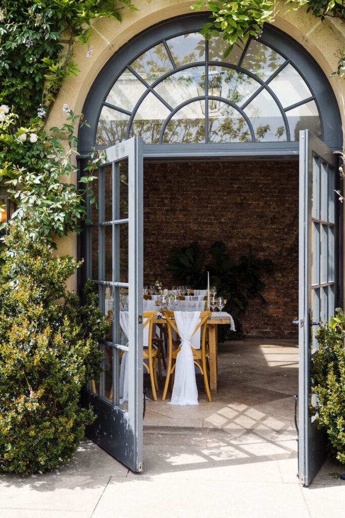Open doors into the Middleton Lodge orangery, framed by greenery, with wedding tables set inside.
