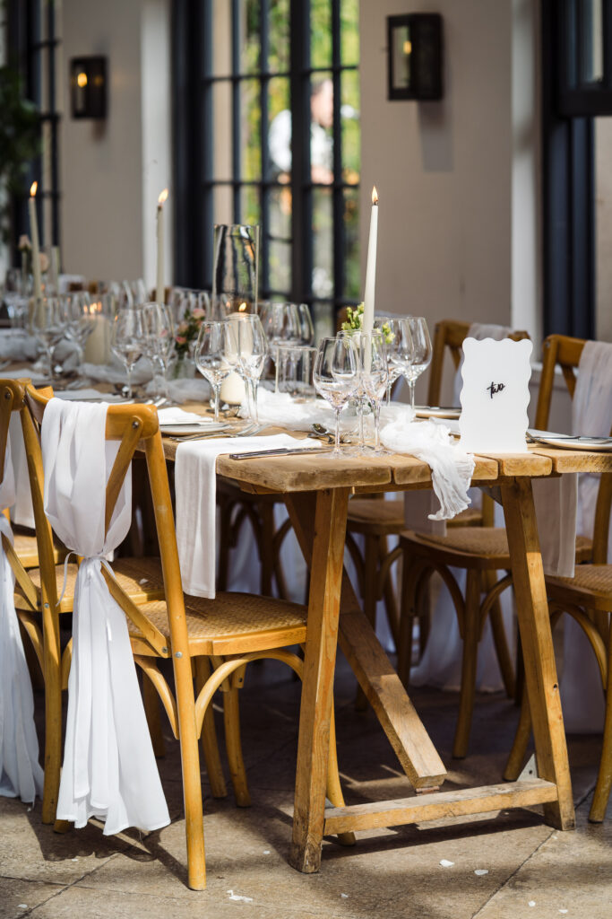 Detail of Middleton Lodge dining tables with wooden chairs, white fabric draping, candles and glassware in the orangery.